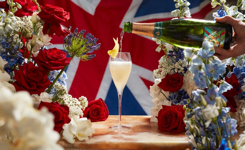 Champagne being poured into a cocktail surrounded by red, white and blue flowers